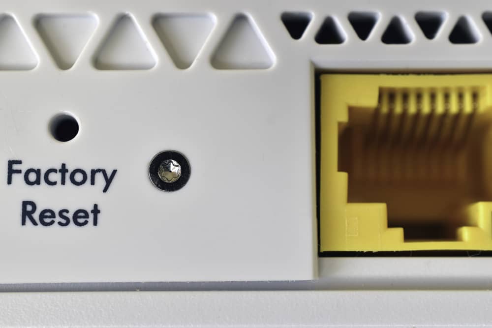 Primer plano del botón reset del router para cambiar dirección IP, mostrando el pequeño orificio para restaurar el equipo.